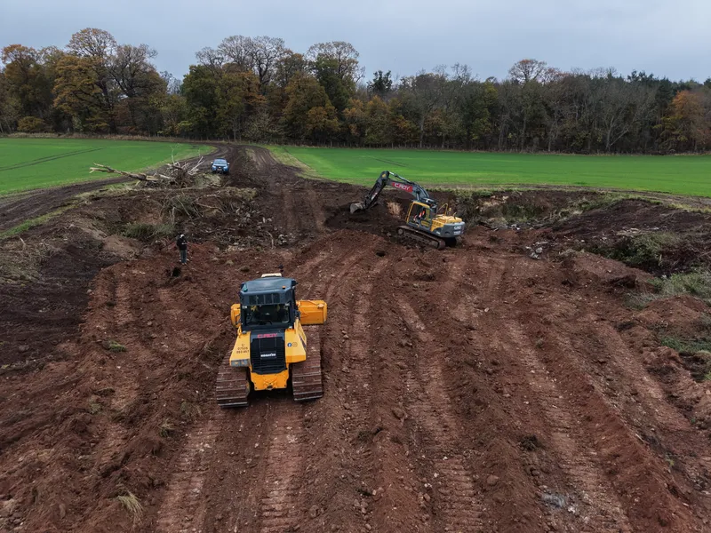 Tracked dumper and excavator shifting spoil in a field